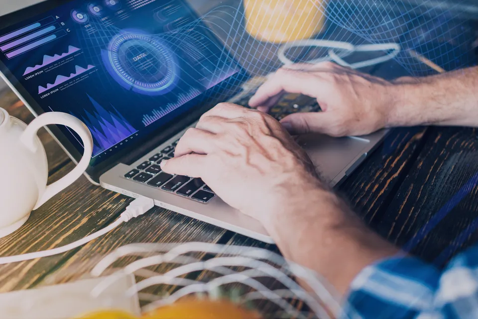 Mãos digitando em um notebook com gráficos na tela